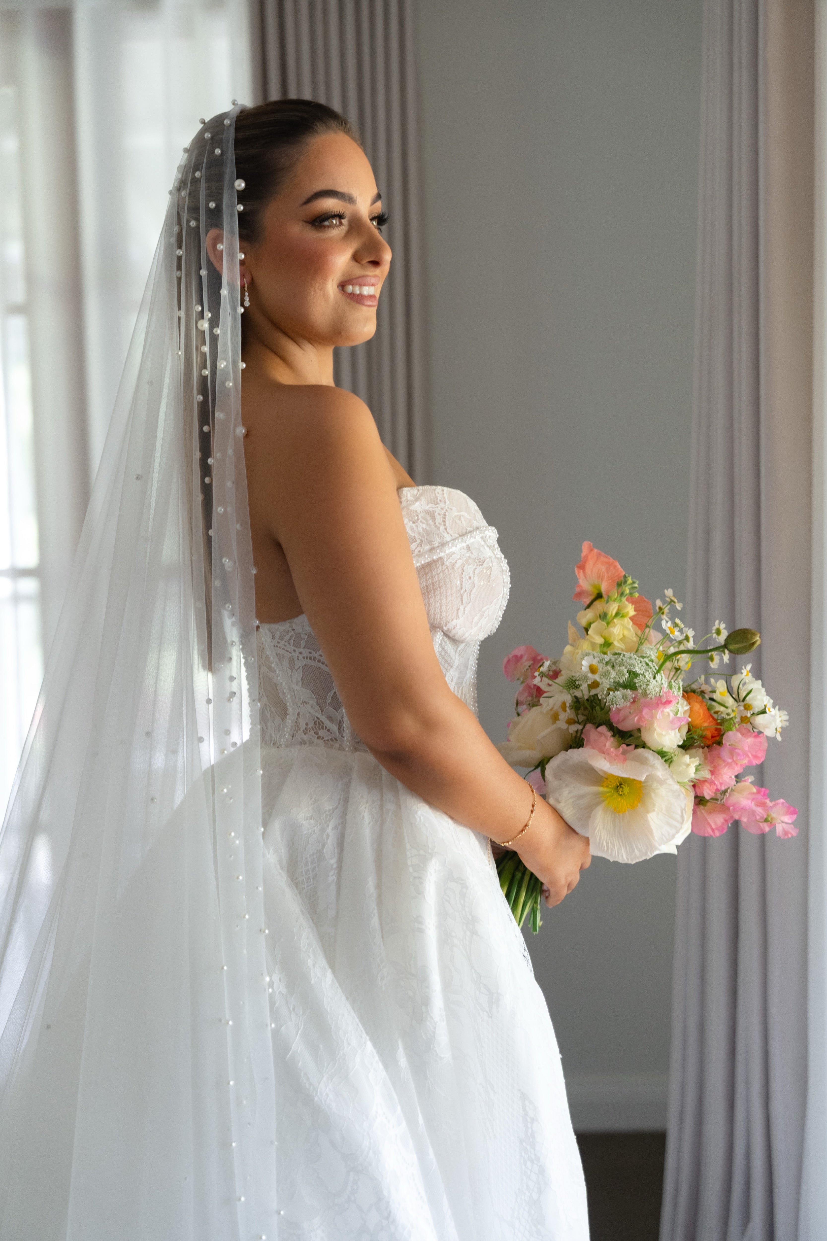 Bride in a white dress holding a bouquet of flowers indoors.