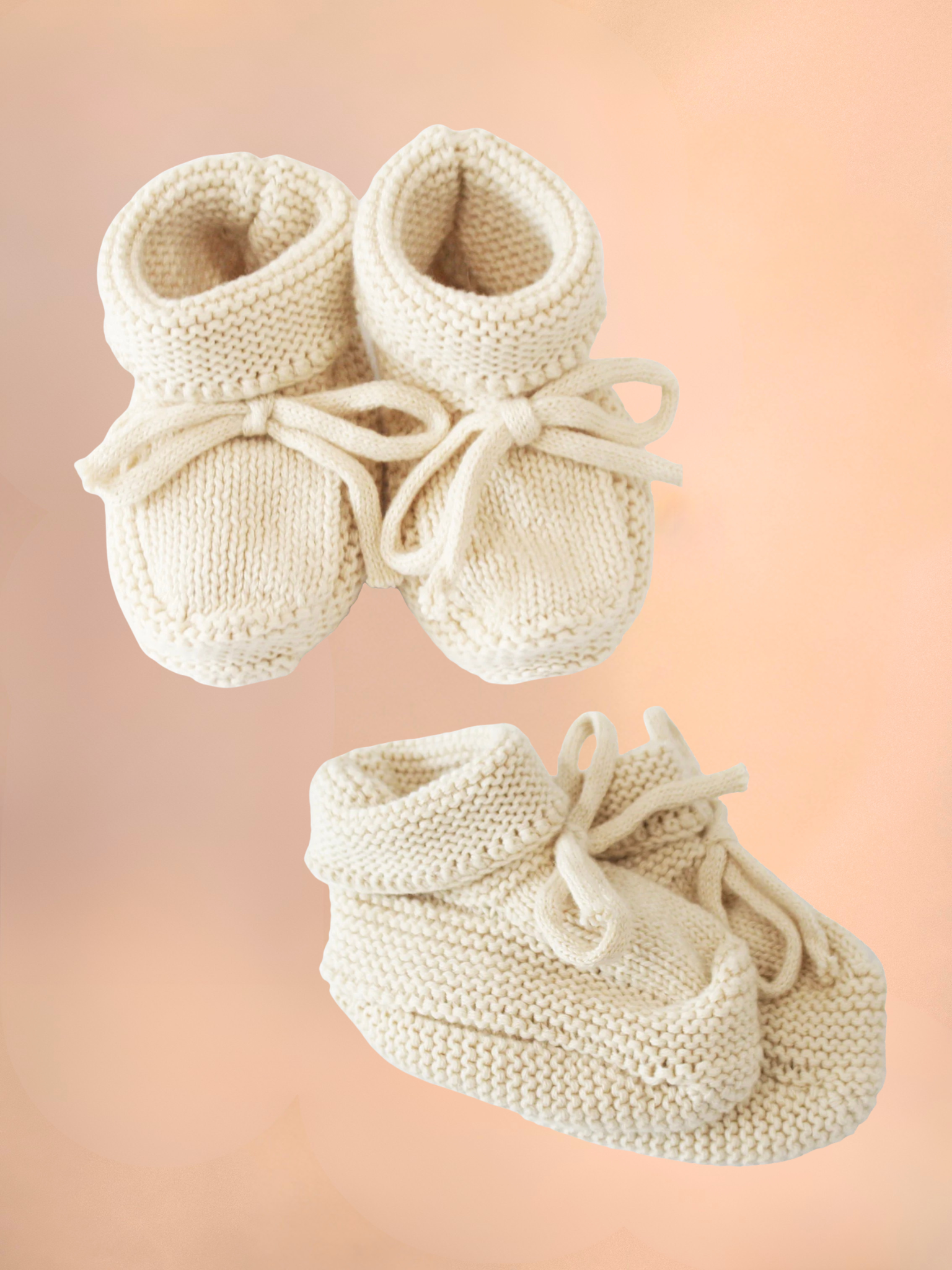 Pair of white knitted baby booties on a soft pink background