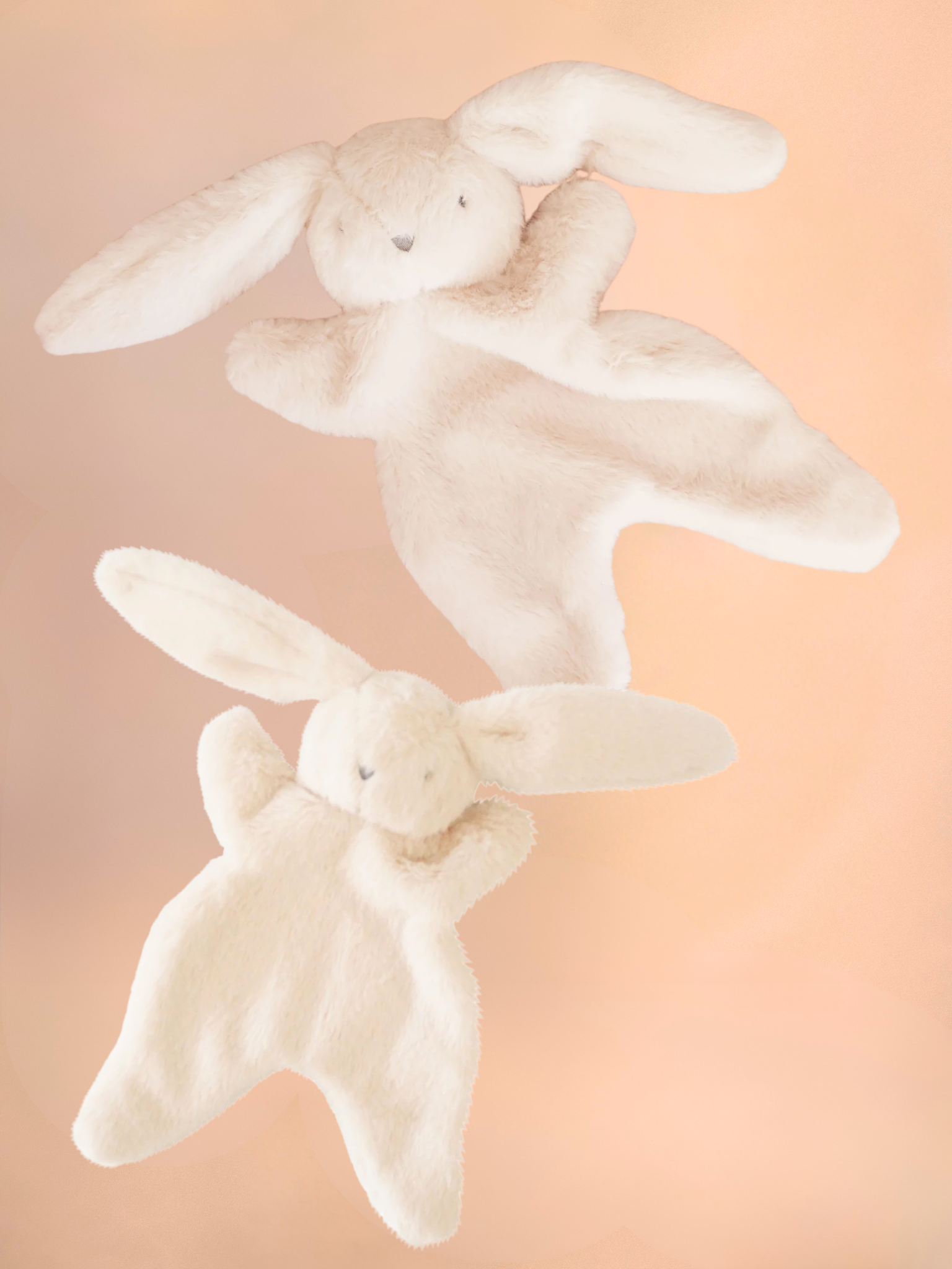 Two white plush bunny toys on a soft pink background