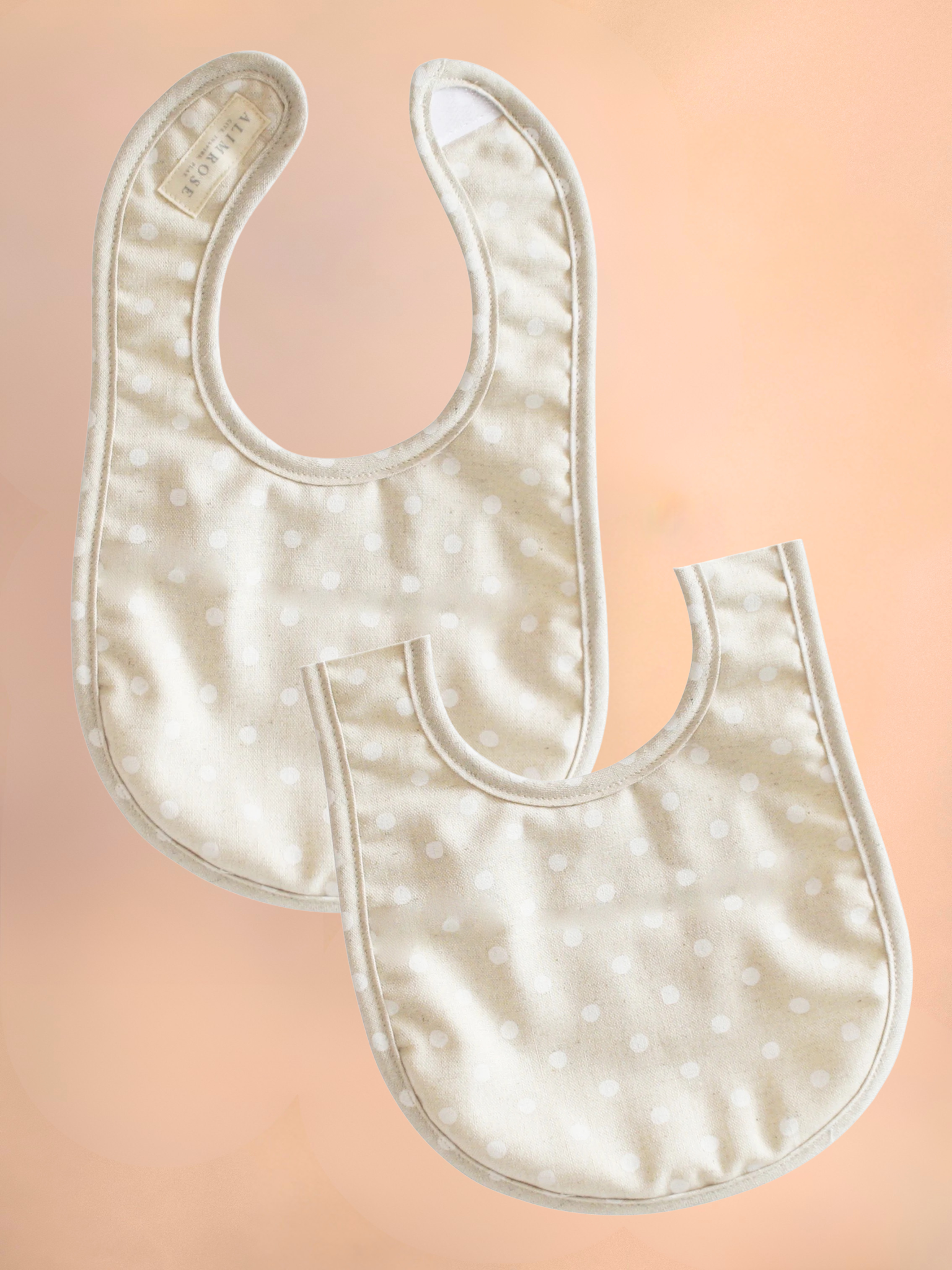 Two white baby bibs on a peach background