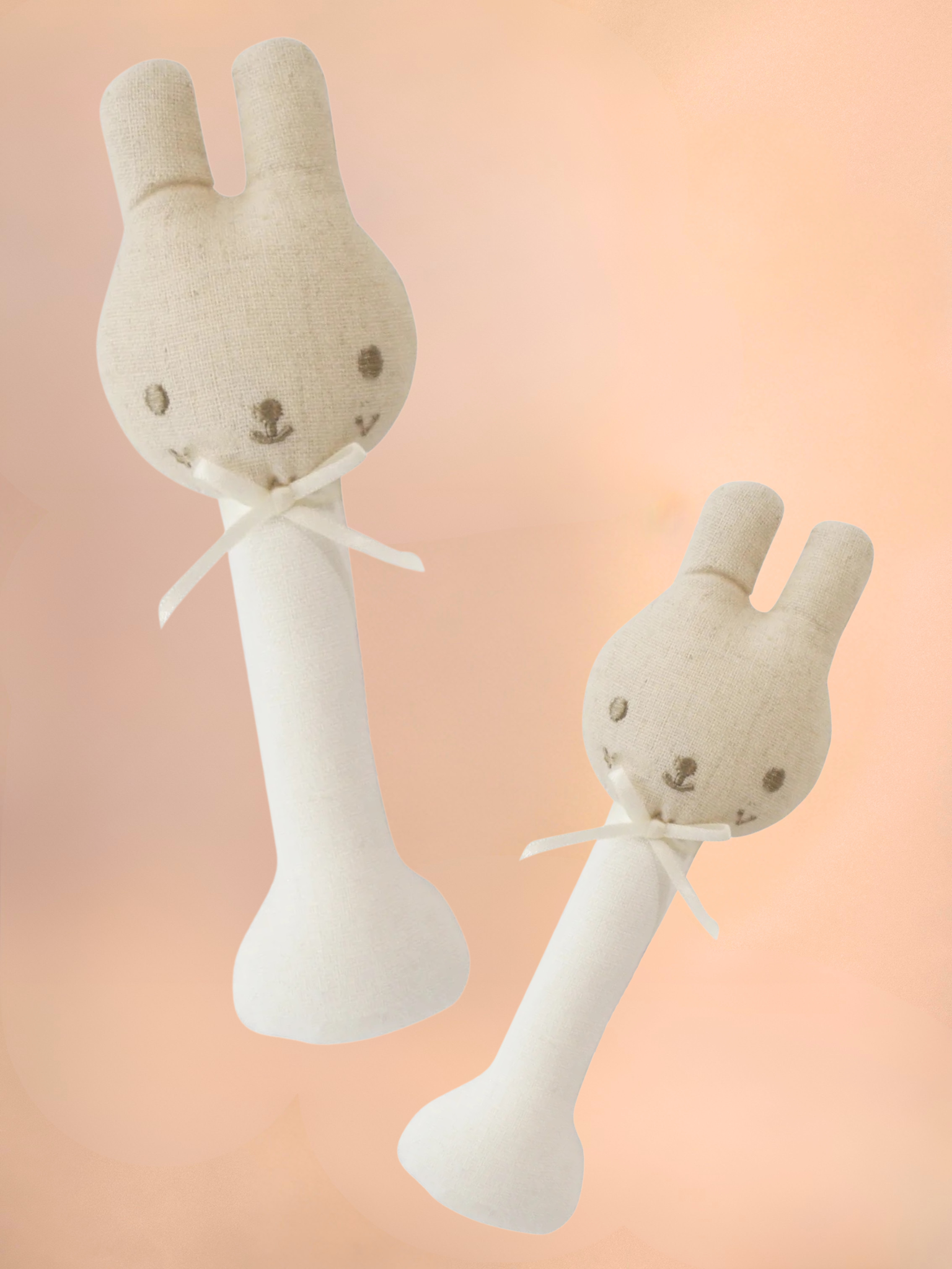 Two plush rabbit toys with white ribbons on a peach background